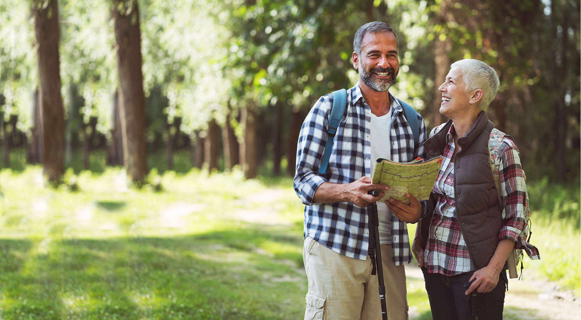 Elderly couple smiling while holding a map in the outdoors